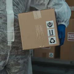 Handler in protective suit carrying a labelled cargo box